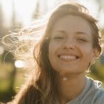 A radiant woman smiling in the sunlight with hair gently blowing outdoors.